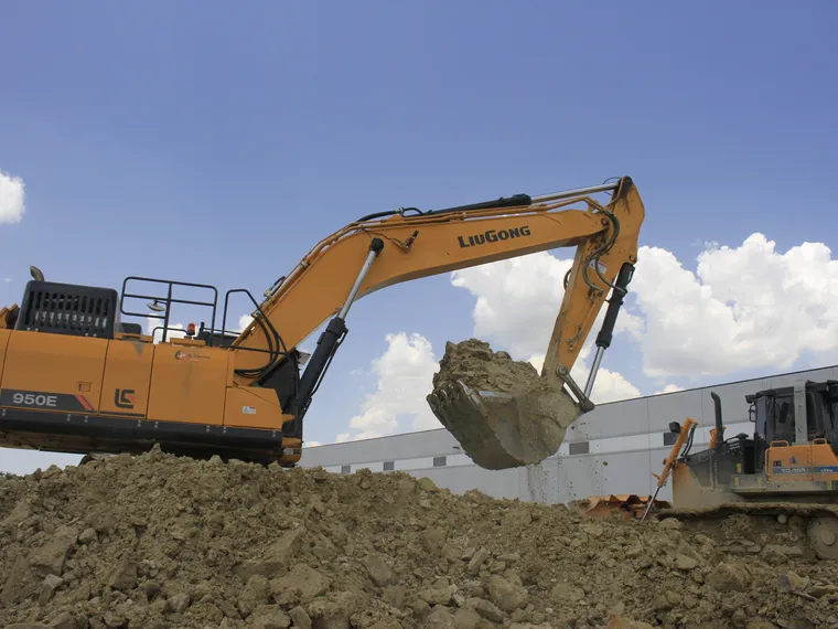 Excavadora LiuGong 950E cargando material con cielo azul junto a una nave